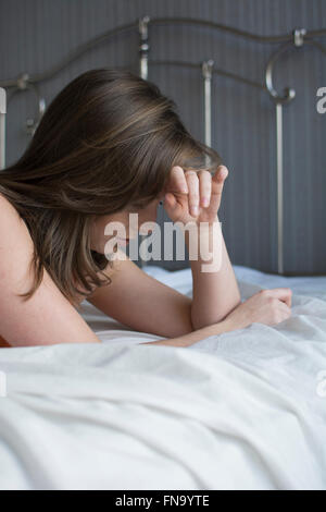 Jeune femme déprimée head in hands in bed Banque D'Images