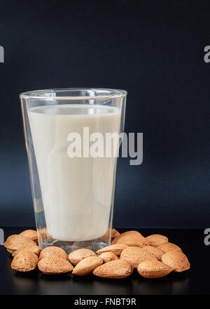 Le lait d'amande dans une double paroi isolés - verre à boire avec des graines d'amandes en coque sur un tableau noir contre fond bleu foncé Banque D'Images