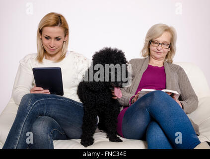 Jeune femme et sa mère assise sur un canapé blanc avec leur caniche noir. Banque D'Images