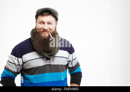 Homme barbu souriant à cap et écharpe avec la cigarette sur fond blanc Banque D'Images