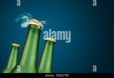 Photo horizontale de trois bouteilles de bière froide avec de l'eau chute et golden cap ouvert sur fond bleu Banque D'Images