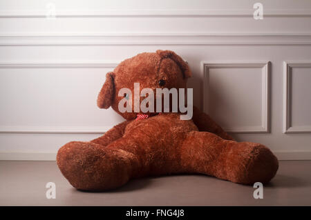 Grand ours en peluche avec un archet en pointillés sur le sol contre le mur blanc d'une salle vide Banque D'Images