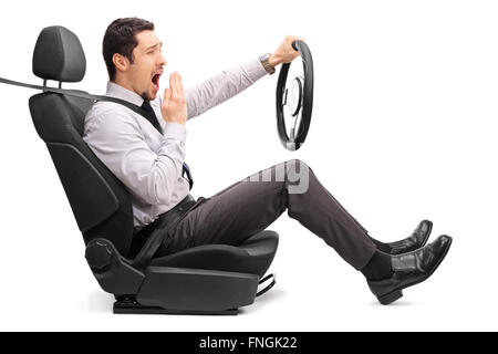 Photo de profil d'un jeune homme endormi tenant un volant assis sur un siège de voiture isolé sur fond blanc Banque D'Images