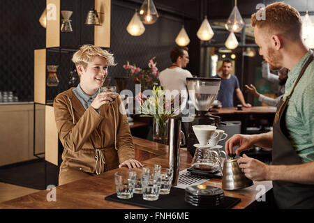 Young woman smiling tandis qu'un barista rend certains café filtre Banque D'Images