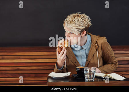 Jeune femme prenant piqûre d'un croissant dans un café moderne Banque D'Images