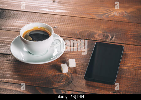 Belle nouveau noir téléphone mobile, une tasse de café avec deux morceaux de morceaux de sucre sur l'ancien fond de bois Banque D'Images