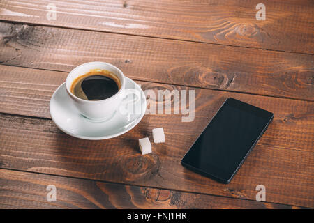 Belle nouveau noir téléphone mobile, une tasse de café avec deux morceaux de morceaux de sucre sur l'ancien fond de bois Banque D'Images