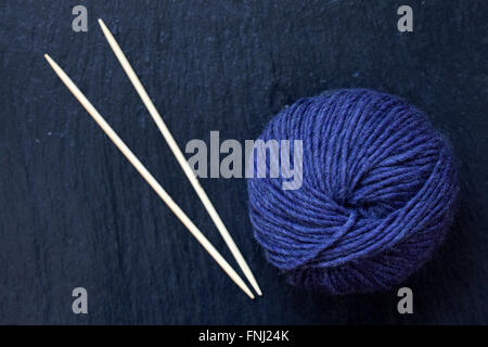 Pelote de fil violet avec des aiguilles à tricoter en bambou avec fond en ardoise noire Banque D'Images
