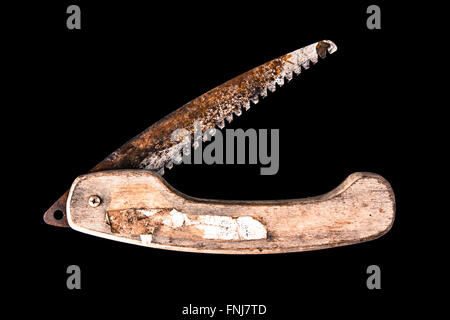 Scie d'élagage pliante rouillée avec un manche en bois et ouvert isolé sur un fond noir Banque D'Images