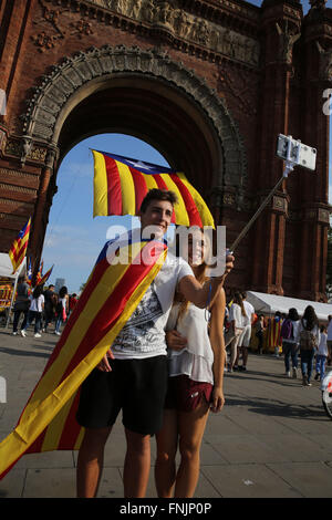 Sep 11, 2015 - Barcelone, Espagne - un jeune couple de prendre des photos avec un bâton et selfies cellphone comme personnes mars portant le drapeau catalan de l'Arc de Triomf de Barcelone. Barcelone a été une mer de rouge et jaune comme la foule portant des drapeaux séparatistes ont défilé dans la ville pour célébrer la fête nationale catalane. Les organisateurs espéraient attirer au moins 500 000 personnes pour un rassemblement en faveur de l'indépendance en utilisant le slogan "Nous allons commencer la construction d'un nouveau pays". L'ESTELADA Drapeau ou "Lone Star" est un drapeau non officiel généralement pilotés par des séparatistes catalans pour exprimer leur soutien à l'indépendance de la Catalogne. (Crédit de droit Banque D'Images