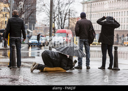 Les sans-abri est mendiant mendier avec parapluie sous la pluie près d'une passerelle à une rue principale de Sofia. La Bulgarie est l'un des plus pauvres co Banque D'Images