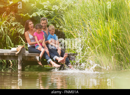 L'été, portrait d'une famille heureuse assise sur le bord d'un ponton en bois, les pieds dans la rivière et faire des projections Banque D'Images