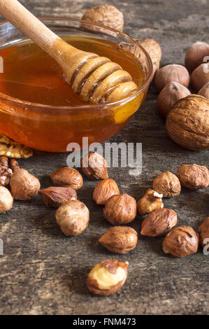 Le miel d'abeilles dans un bocal en verre, de noisettes et de noix, sur une vieille table en bois vintage. La saine alimentation concept de style. Focus sélectif. Banque D'Images