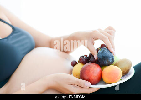 Pregnant woman holding fruits sur une assiette en face de son ventre Banque D'Images