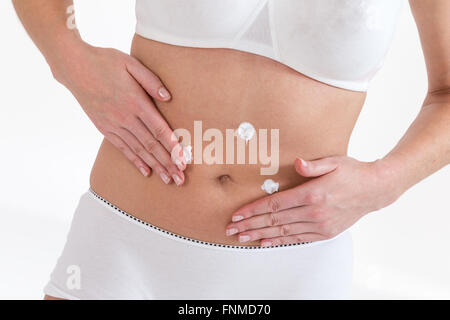 Appliquer la crème corporelle femme isolée sur l'abdomen fond blanc Banque D'Images