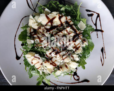 Assiette de salade et copeaux de fromage concerné en assaisonnement balsamique sur une plaque en céramique blanche Banque D'Images