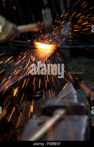 Blacksmith façonner un morceau de fer chaud sur l'enclume avec un marteau, avec des étincelles voler. Banque D'Images