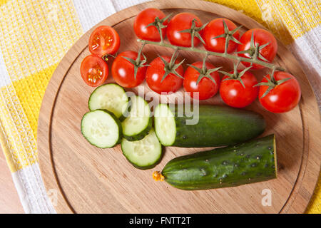 Les concombres et tomates cerises coupées en tranches sur une planche en bois Banque D'Images