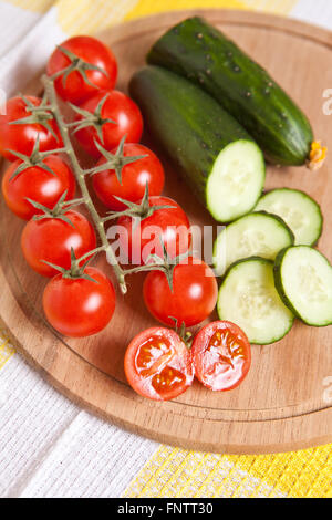 Les concombres et tomates cerises coupées en tranches sur une planche en bois Banque D'Images