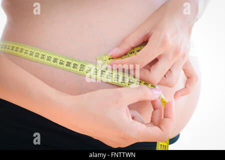 Femme avec un ventre de la grossesse elle-même de mesure avec un mètre à ruban jaune Banque D'Images