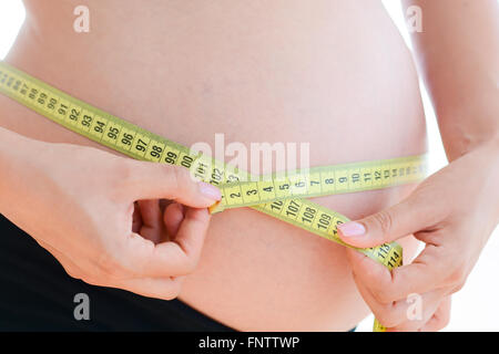 Femme avec un ventre de la grossesse elle-même de mesure avec un mètre à ruban jaune Banque D'Images