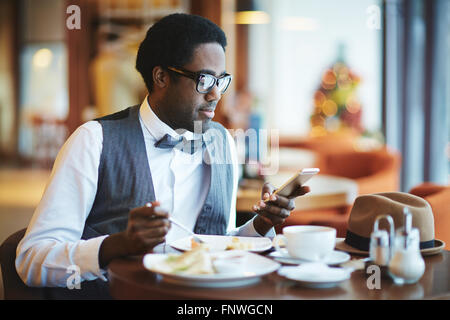 Jeune homme élégant avec cellphone manger en cafe Banque D'Images