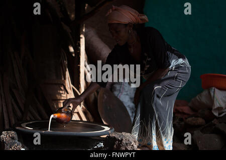 Une femme verse de l'huile de noix de coco sur un incendie lire pour faire un pain plat populaire de l'Injera en Ethiopie. Banque D'Images