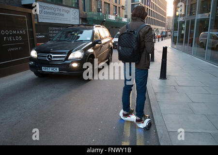 L'homme sur son trajet passe d'hoverboard autres trafic allant dans la direction opposée. Londres, Angleterre, Royaume-Uni. Un auto-équilibrage du deux roues, ou scooter électrique auto-équilibré, aussi communément appelé un Hoverboard, est un type de batterie rechargeable, portable-scooter. Ils se composent généralement de deux roues disposées côte à côte, avec deux petites plateformes entre les roues, sur laquelle l'avenant est. L'appareil est contrôlé par le cavalier, Debout les pieds sur l'gyroscopiques tampons avec. Banque D'Images