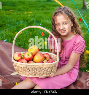 Fille assise sur le sac dans le parc avec un panier de pommes Banque D'Images