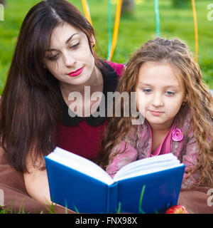 Mère et fille lire un livre allongé sur le plaid dans le parc Banque D'Images