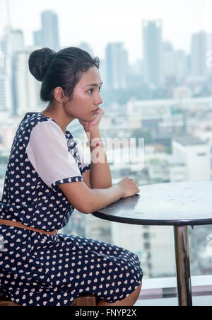 Jeune femme assise à une table près de la fenêtre dans un gratte-ciel Banque D'Images