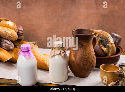 Deux bouteilles en verre de lait, de hautes maisons pitcher, petite tasse et pains en arrière-plan sur la table Banque D'Images