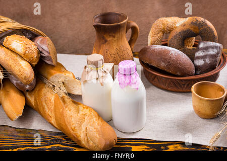 La bouteille de lait en verre recouvert de tissu, de hauteur de pitcher et tasse à côté de miches de pain et bagels Banque D'Images