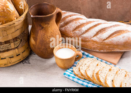 Pichet en bois unique, pleine tasse de lait et du pain, avec du pain et des tranches entières à côté de panier sur le tableau Banque D'Images