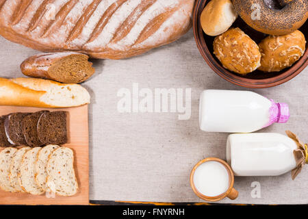 Vue du haut vers le bas d'un assortiment de pains, petits pains, bagels, tranches et lait, tasse et bouteilles sur tissu sur table en bois avec copie espace. Banque D'Images