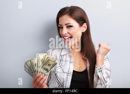 Happy young casual woman holding dollars et montrant des signes de réussite oui avec la bouche ouverte sur fond bleu Banque D'Images