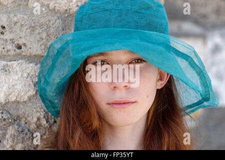 Fille aux cheveux roux avec un chapeau de soleil turquoise à sérieusement, portrait, Italie Banque D'Images