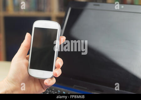 Femelle est titulaire d'un téléphone cellulaire, ordinateur portable ouvert avec un écran est sombre en arrière-plan. Toutes les marques potentiels sont enlevés. Banque D'Images