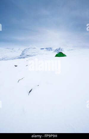 Une tente nichée dans la neige des collines de Torridon en hiver avec Beinn dix-huit comme toile de fond, depuis le sommet de Beinn a' Chearcaill Banque D'Images