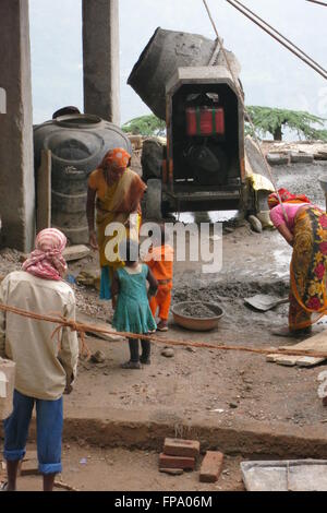 Une femme sur un site de travail indien prend une pause momentanée du mélange de béton pour répondre à ses petits enfants Banque D'Images