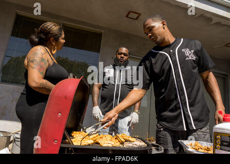 17 mars 2016 - Roberto 'News'' Smith (à droite) de poulet grills à Compton, Californie comme DJ Kev (centre) attend les commandes de livraison. Malachie 'Spank'' Jenkins, aÂ Crip, et Roberto 'News'' Smith de la Pirus (Sang) a commencé la cuisine piège les gangs de L.A. en 2013, après avoir rencontré grâce à des amis communs et qui veulent aller legit. Ils ont renoncé à frapper des gangs et le trafic de drogue d'exécuter leur restaurant souterrain à partir d'un petit home cuisine, offrant des repas comme à la Compton pour les quartiers et les communes limitrophes du centre-sud de Los Angeles. Le piège Cuisine (un piège à House, un terme argotique Banque D'Images