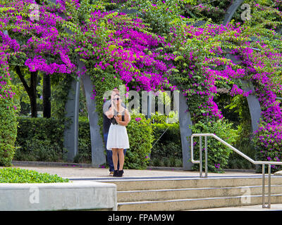 Beau couple avec femme à l'aide de téléphone dans une scène florale lumineuse sur South Bank Brisbane, Queensland, Australie Banque D'Images