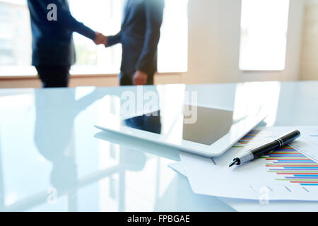 Tablette numérique avec des documents sur la table avec des hommes d'affaires derrière Banque D'Images