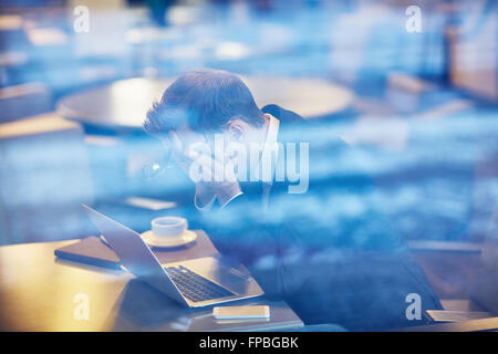 Souligné businessman sitting in front of laptop in cafe Banque D'Images