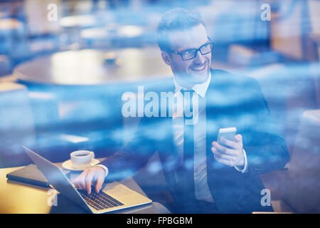 Young smiling woman sitting at café avec ordinateur portable et smartphone Banque D'Images
