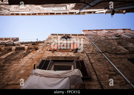 Vue vers le ciel entre deux bâtiments anciens dans une étroite rue de Dubrovnik, avec lave-linge suspendu à une des fenêtres. Banque D'Images