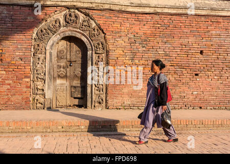 Le Népal, Patan. Nepali Woman Walking par portes de palais royal composé, Durbar Square. Banque D'Images