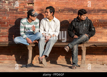 Le Népal, Patan. Trois jeunes hommes népalais assis sur un banc à Durbar Square, le port de vêtements occidentaux. Banque D'Images