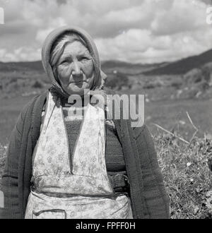 Années 1950, historique, un portrait par J Allan Cash d'une femme irlandaise mûre dans un robe chasuble, un gilet et un foulard, assis par un hedgerow dans la campagne, à l'ouest de l'Irlande. Banque D'Images