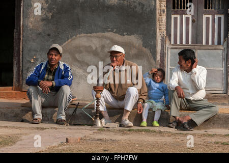 Le Népal, Patan. Les hommes de détente sur trottoir, l'un fumeur Pipe de l'eau. Banque D'Images